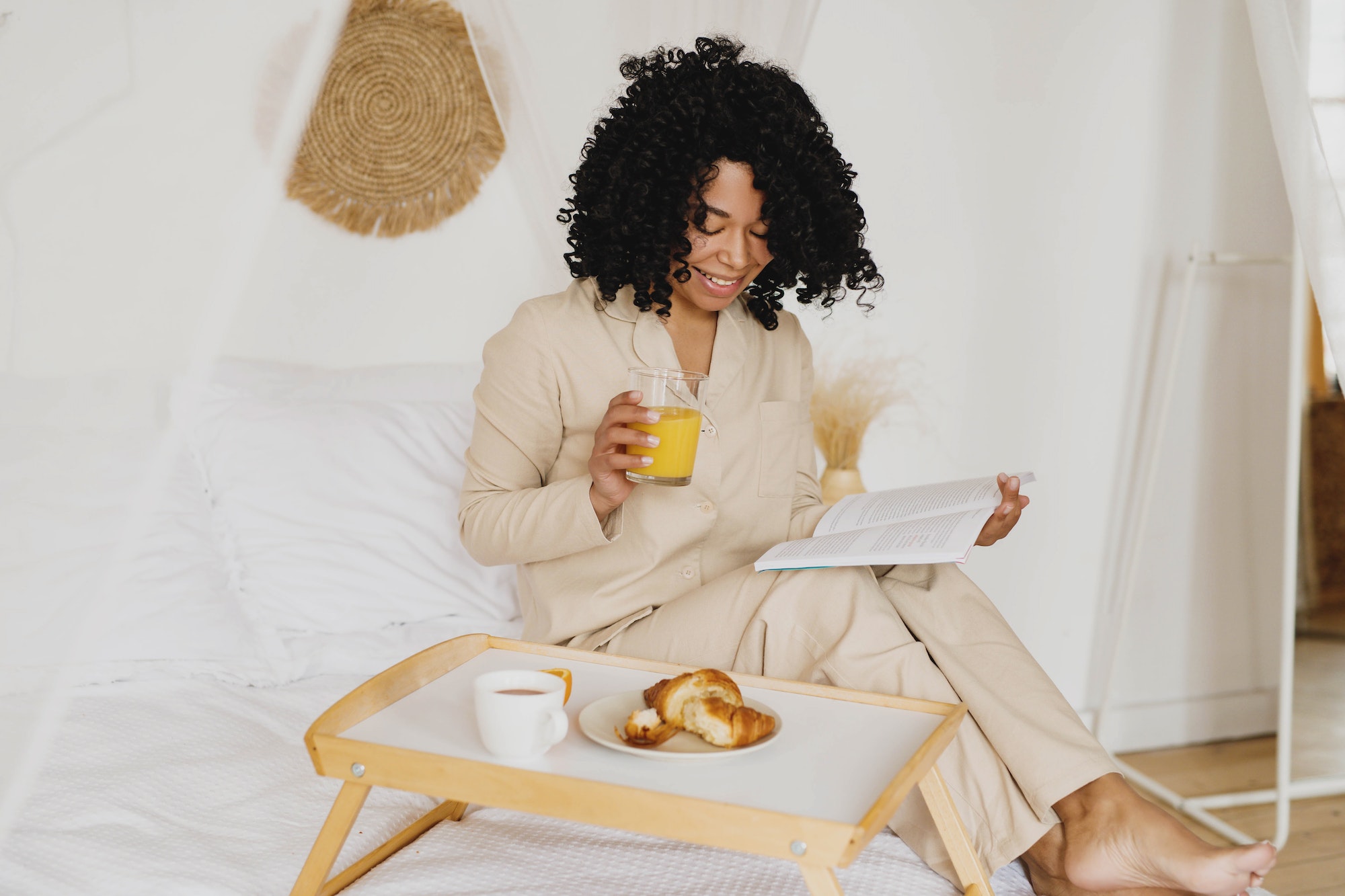 Young African American woman reading and having breakfast in bed.