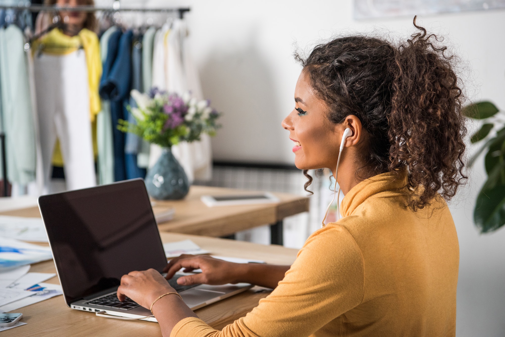 beautiful smiling young african american woman in earphones using laptop with blank screen