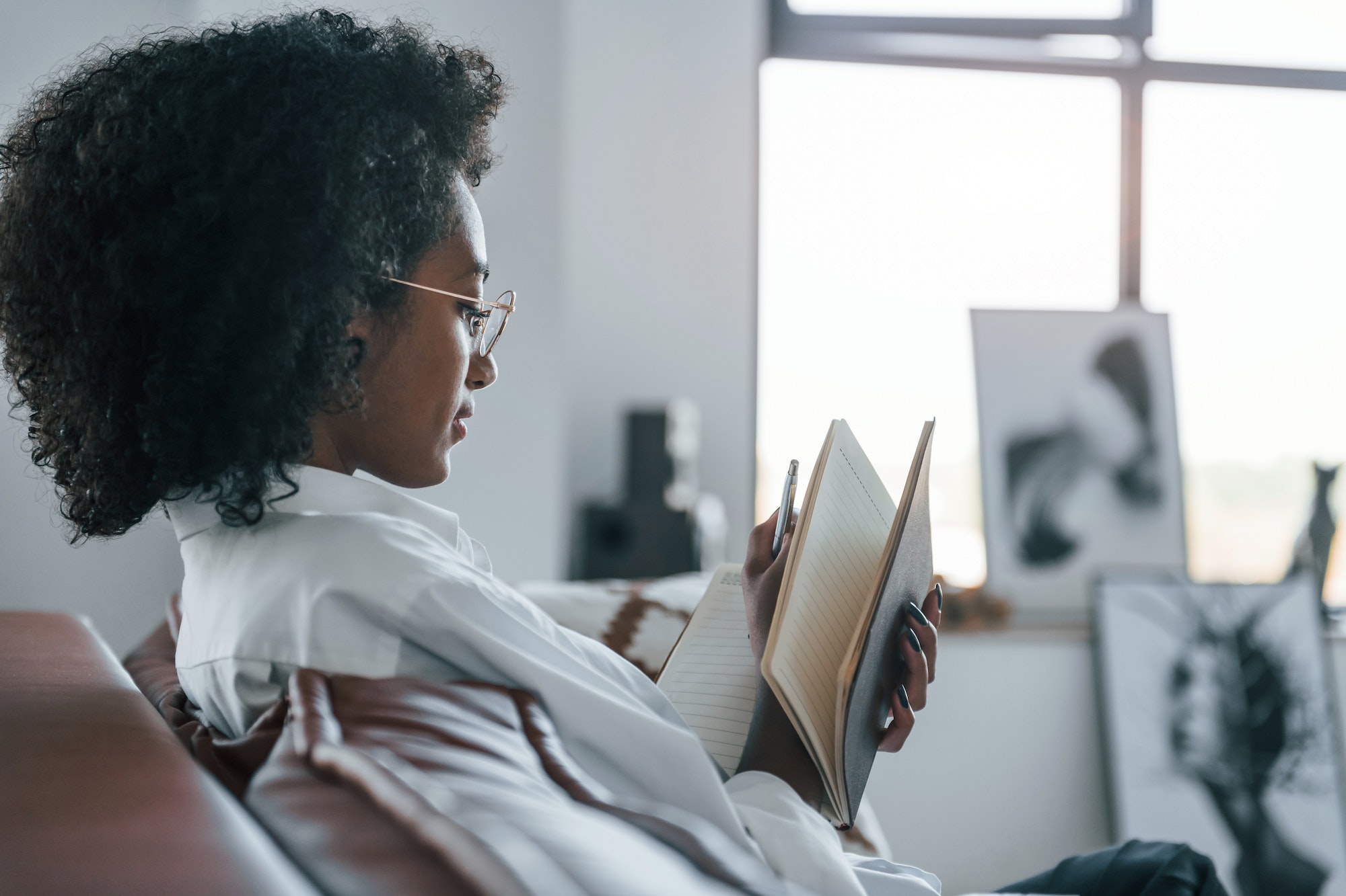 Holds notepad. Young african american woman with curly hair indoors at home